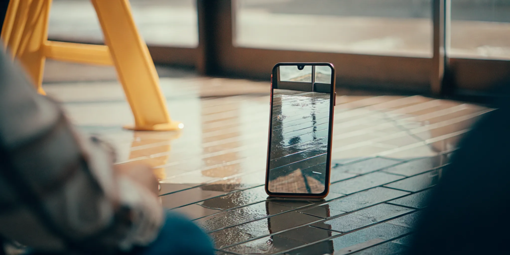 A smartphone on a tiled floor displaying a photograph of a wet floor hazard, showing slip and fall evidence preservation